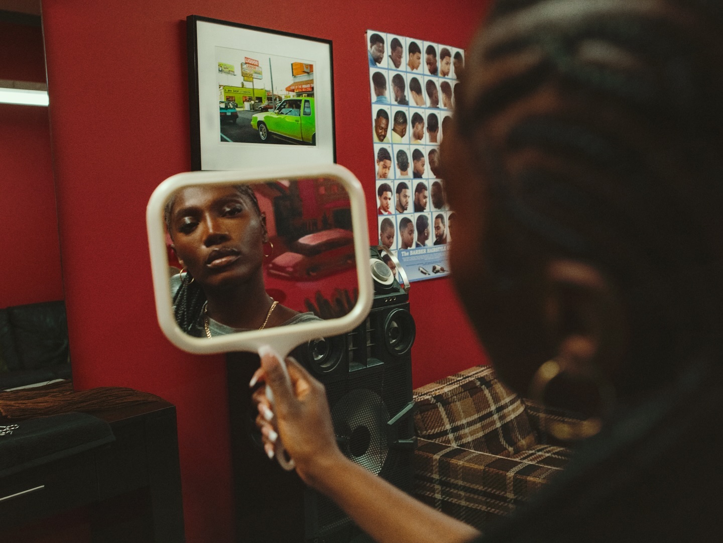 Woman looking into a handheld mirror in a red-walled barbershop