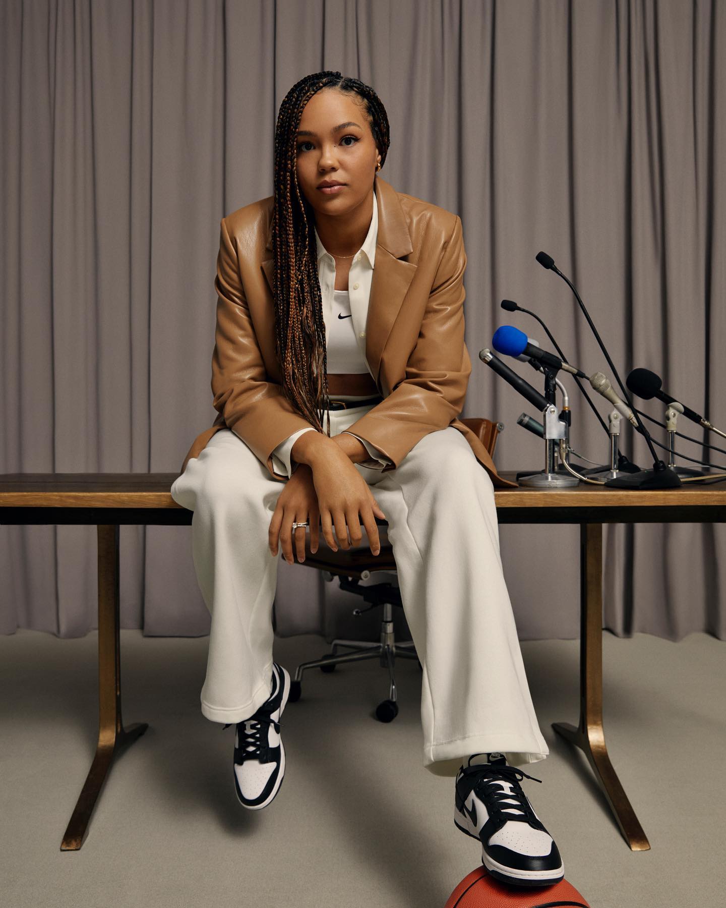 An athlete seated on a press conference table with a sneaker resting on a basketball